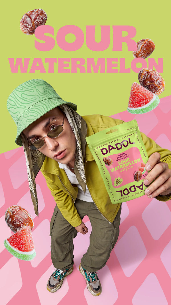 Young man wearing a green patterned bucket hat and sunglasses holding a DADDL Sour Watermelon candy dates pouch while posing against a green and pink background with large “SOUR WATERMELON” text, floating coated dates, and watermelon gummy candies.