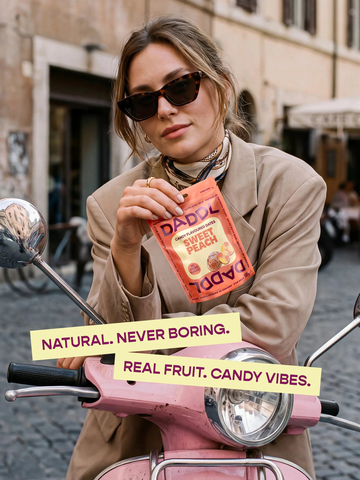 Kvinna på en rosa vespa med en påse Sweet Peach. Text: Natural. Never boring. Real fruit. Candy vibes.