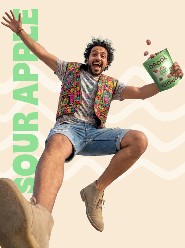 Person jumping joyfully with a bag of Sour Apple Dandies candy, set against a light beige background.