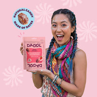 Woman holding a DADDL strawberry milkshake package against a pink background with DADDL branding.